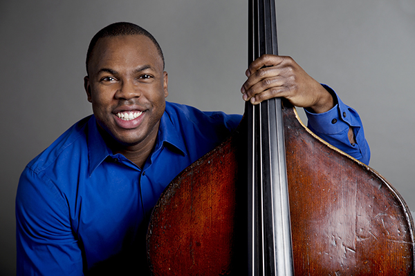 Joseph Conyers smiles at the camera while holding his double bass at his side.
